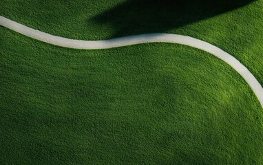 High-angle close-up view of artificial turf with a meandering white line. The texture of the green turf is visible, and a shadow is cast across part of the surface
