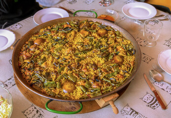 Authentic Valencian paella served in a large traditional paella pan ready to serve on a table with empty plates.
