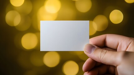 Hand Holding Blank Frosted Business Card with Rounded Edges Against Blurred Golden Bokeh Background