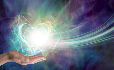 Male healer sending love vibes - distant healing theme with a male open palm and a wispy heart shaped energy ball against a beautiful misty energy background with copy space for spiritual message
