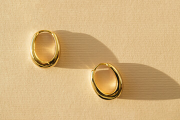 Gold earrings closeup on pastel background with shadow. Concept of stylish women's accessories