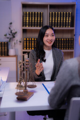 Asian female lawyer explaining contract details to client in law firm office with scale of justice and law books in background, legal consulting and disputing, lawyer and client meeting concept