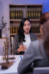 Asian lawyer holding a pen while advising a client during a meeting in the office, surrounded by law books and a scale of justice on the desk, illustrating professional legal consultation