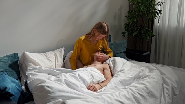 Couple relaxing together in bedroom at home, man and woman laying in bed, man resting on woman's legs, talking gently touching and smiling. - Powered by Adobe