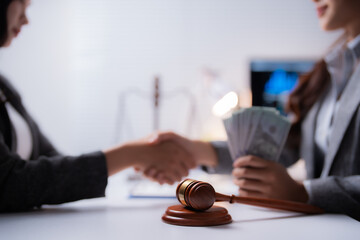 Two businesswomen shaking hands after reaching a bribery agreement involving money and a judge's gavel, symbolizing corruption and illegal dealings in the business world