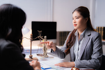 Asian female lawyer pointing at a contract while discussing an agreement with a client in an office, featuring scales of justice and a gavel on the table, exemplifying legal consultation