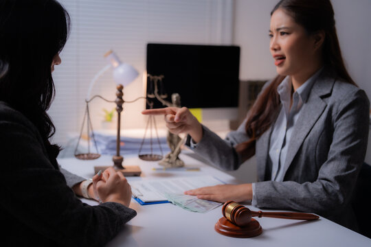 Asian female lawyer pointing finger and scolding client during a meeting in office with scales of justice, gavel and paperwork on the table