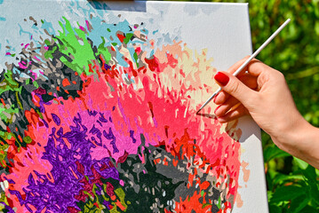 A vibrant painting displayed outdoors, placed on an easel amidst a beautiful natural landscape,...