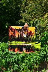A vibrant painting displayed outdoors, placed on an easel amidst a beautiful natural landscape,...