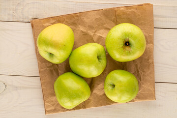 Several sweet green apples with paper bag on wooden table, close-up, top view.