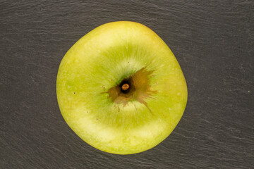One sweet green apple on slate stone, macro, top view.