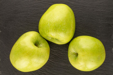 Three sweet green apples on a slate stone, macro, top view.