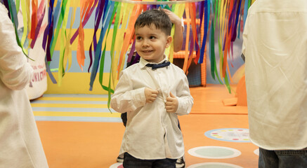 kids are having fun at birthday party in playground room with children's entertainer. happy boys and girls are jumping,playing with colorful ribbons on rope.true emotions on preschoolers face.