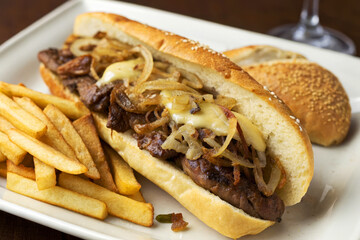 Gourmet Cheesesteak Sandwich with Sauteed Onions and Fries on a White Plate