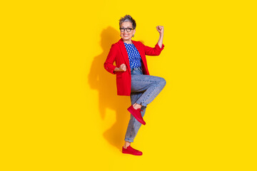Happy mature woman in stylish outfit posing confidently against yellow background, showing dynamic and cheerful gestures