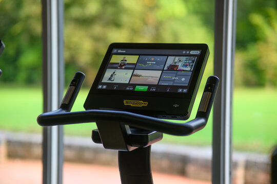 A stationary technogym bike with a screen that shows a variety of exercise videos