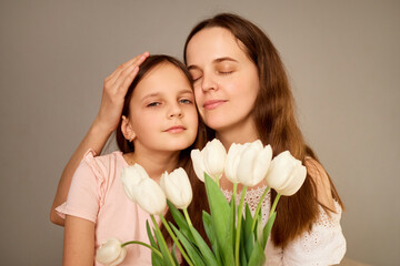 A mother lovingly embraces her daughter as they share a serene moment. The young girl gazes softly...