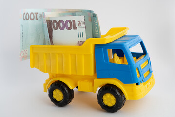 Cash, money, a toy car of yellow and blue colors carries hryvnia banknotes on a white background.