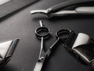 Close-up of essential barber tools including scissors, clippers, and a comb on a dark surface, showcasing the precision instruments used for grooming and hairstyling