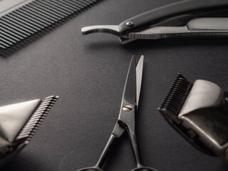 A collection of barbering tools is displayed on a dark surface, featuring scissors, clippers, and combs ready for a grooming session in a salon environment
