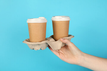 Woman holding holder with paper cups against light blue background, closeup. Mockup for design