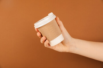Woman holding paper cup on brown background, closeup. Mockup for design