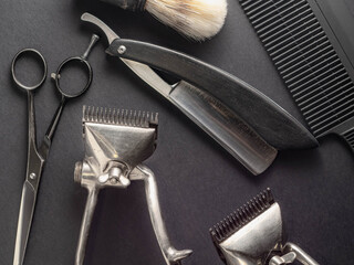 A collection of classic barber tools including scissors, clippers, a straight razor, and a shaving brush on a dark background. This arrangement highlights the artistry of traditional barbering