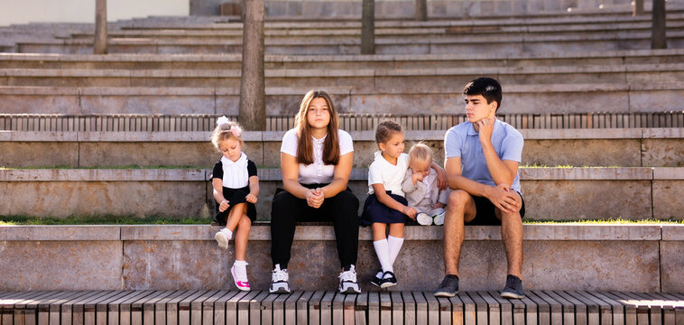 Children of different ages in school uniforms sitting on the steps outside