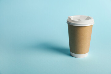 One paper cup on light blue background. Mockup for design