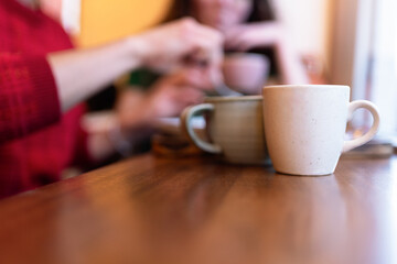 Close up of teacups on wooden table, friends chatting and enjoying time together in background, warm and cozy atmosphere