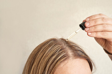 Female applying hair serum with dropper to blonde hair for healthy scalp treatment and nourishment.