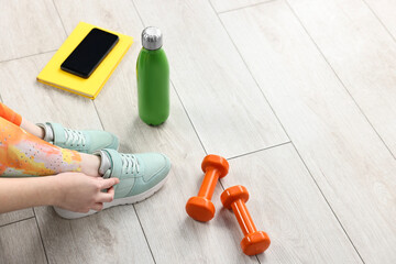 Woman putting on sneakers and gym equipment indoors, closeup. Space for text