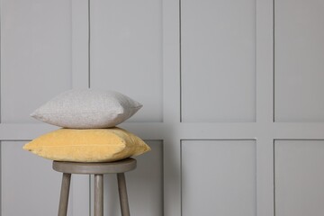 Soft decorative pillows on stool near grey wall. Space for text