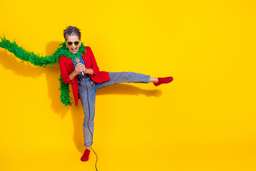 Colorful woman expressing joy and energy in stylish outfit with red jacket and green boa on vibrant yellow background.