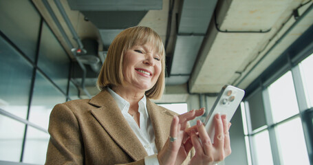 A mature businesswoman using a smartphone in a modern office environment, focusing on professional tasks or communication, highlighting confidence and technological proficiency
