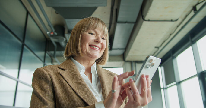 A mature businesswoman using a smartphone in a modern office environment, focusing on professional tasks or communication, highlighting confidence and technological proficiency