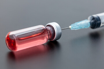 Syringe with red liquid on a black background representing medical injection and healthcare.