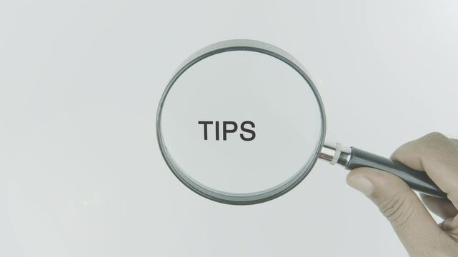 Tips text or word highlighted by a magnifying glass in a hand on a white background, symbolizing helpful advice and guidance for improvement