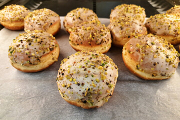 Fresh donuts with pistachio sprinkles on a bakery shelf. Sweet pastries arranged on white parchment paper. Delicious dessert in a pastry shop. Sweet bakery background.