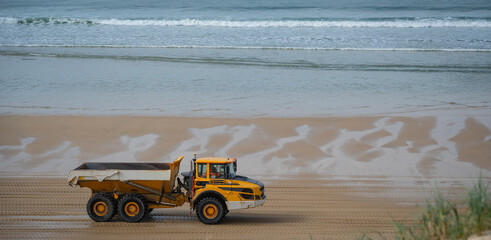 A dump truck carries loads of sand along the biscarosse dune coastline. The vehicle works to combat erosion as it traverses the wet, reflective sands near the ocean.