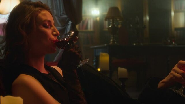Two vampire lovers clinking glasses of red blood in celebratory toast in dimly lit, vintage-gothic room