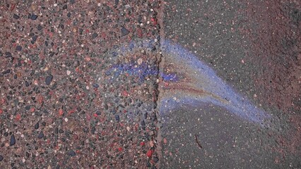 Smuges of Petrol Toxic Substance Spill on Wet Asphalt Surface Creating Colorful Rainbow through...