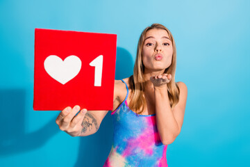 Attractive woman holding a red like notification symbol while blowing a kiss against a vibrant blue...