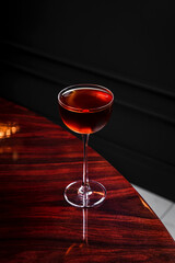 A manhattan cocktail in a coupe glass on glossy wooden table in a bar with copy space