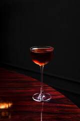 A manhattan cocktail in a coupe glass on glossy wooden table in a bar with copy space
