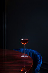A manhattan cocktail in a coupe glass on glossy wooden table in a bar with copy space