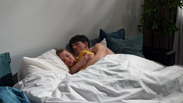 Couple relaxing together in bedroom at home, man and woman laying in bed and sleeping, hugging each other and resting, happy expression. Slow motion