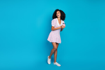 Stylish young woman in a printed dress enjoying a cheerful moment on a vibrant blue background,...