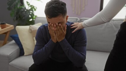 Couple in a cozy living room with man covering face in distress and supportive woman comforting him, creating an intimate emotional atmosphere at home.