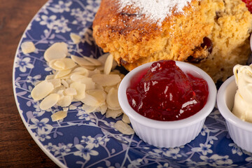 A Cherry Almond Scone with strawberry jam . The jelly is in a white bowl of clotted cream